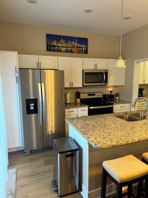 A modern kitchen with white cabinets, stainless steel appliances, granite countertops, and a small trash bin.