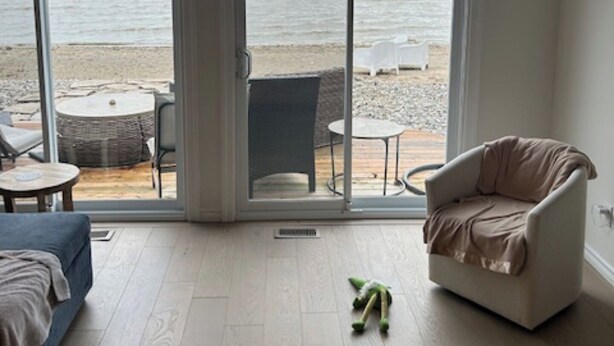 A room with a large sliding glass door leading to a beach view. Inside, there is a bed, a chair, and a small table.