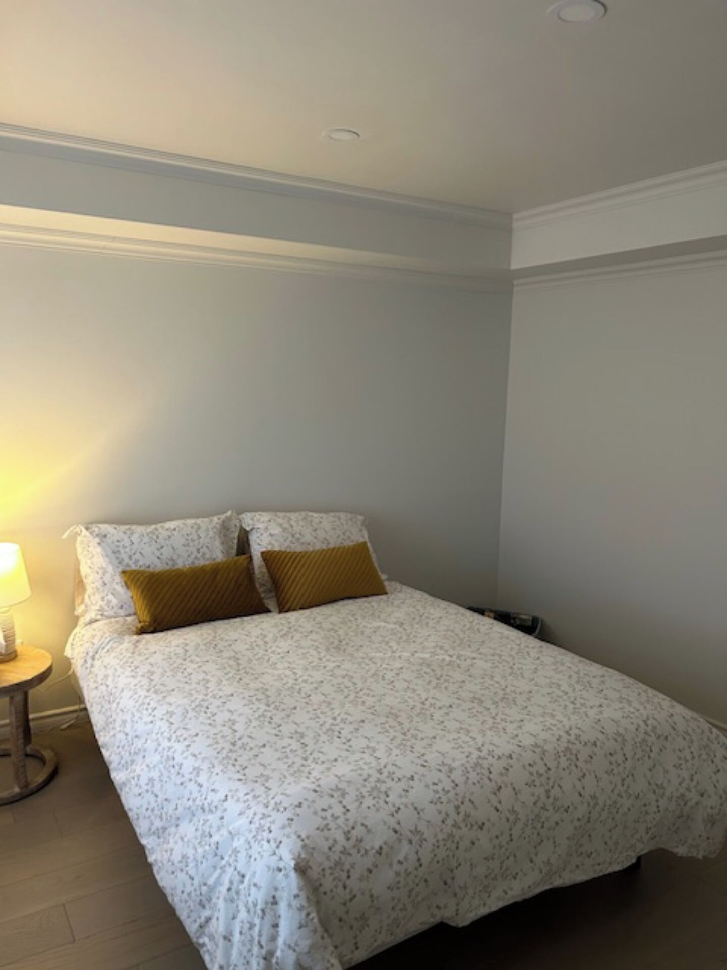 A bedroom with a bed, two pillows, a bedside table with a lamp, and a wooden floor.