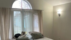 A bedroom with a bed, a window with curtains, a ceiling fan, and a wall-mounted light.