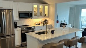 A modern kitchen with white cabinetry, stainless steel appliances, and a central island with bar stools.