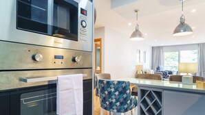 Une cuisine moderne dotée d’appareils électroménagers en acier inoxydable, un coin repas avec des chaises à motifs et un éclairage suspendu.