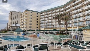 Ein Hotel mit Poolbereich, Sitzgelegenheiten im Freien und mehreren Balkonen.