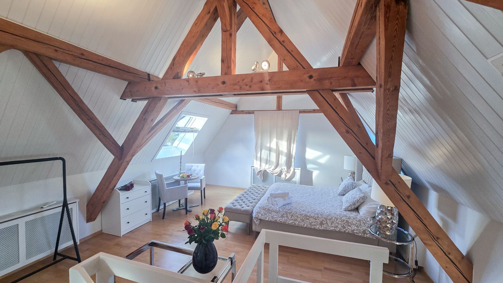 A high-ceilinged attic bedroom with a loft-style bed, a dining area, and a skylight.
