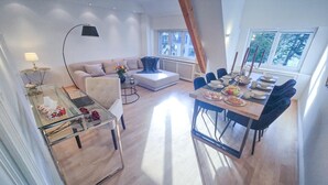 Una sala de estar moderna con una mesa de vidrio para comer, un sofá y una mesa de centro. Se ve una ventana con vistas a árboles.