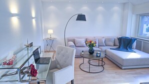 Una sala de estar moderna con un escritorio de vidrio, una computadora portátil, un sofá, una mesa de centro y una lámpara de pie.