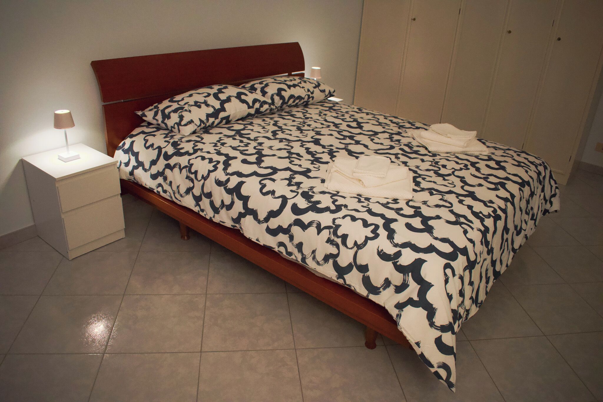 Un lit bien fait, avec une couvre-lit à motifs, une lampe de chevet et une table de nuit.