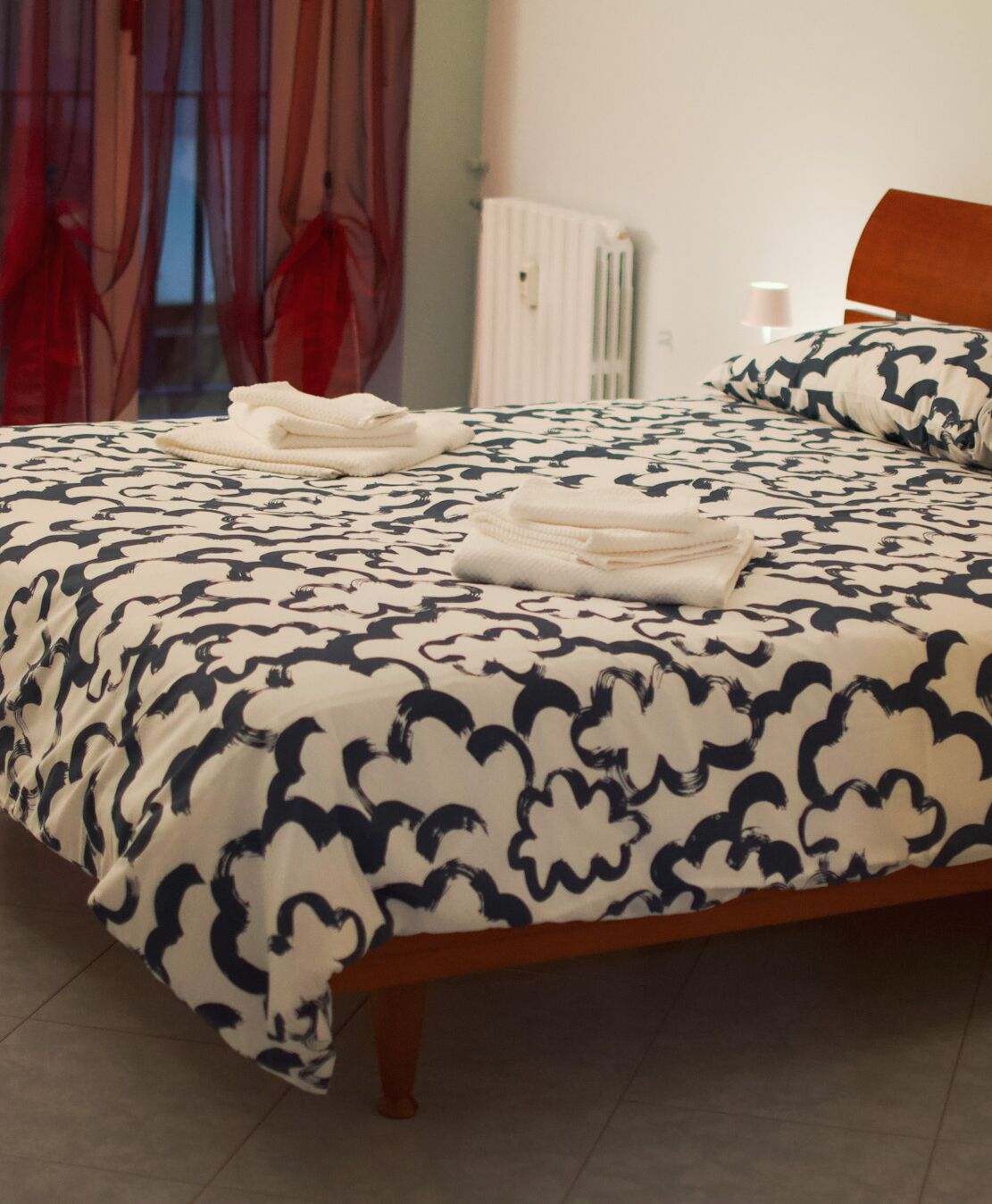 A neatly made bed with a patterned bedspread, a wooden headboard, and a white radiator in the background.