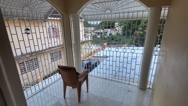 A room with a view through a barred window, a tiled floor, and a wooden chair. - Charming 3-bedroom house with AC, WiFi in delightful Savanna La Mar (Savanna La Mar)