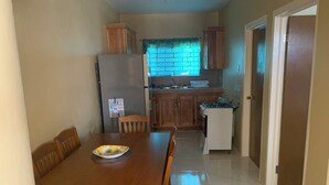 A compact kitchen with wooden cabinets, a refrigerator, a stove, and a dining table with chairs. - Charming 3-bedroom house with AC, WiFi in delightful Savanna La Mar (Savanna La Mar)