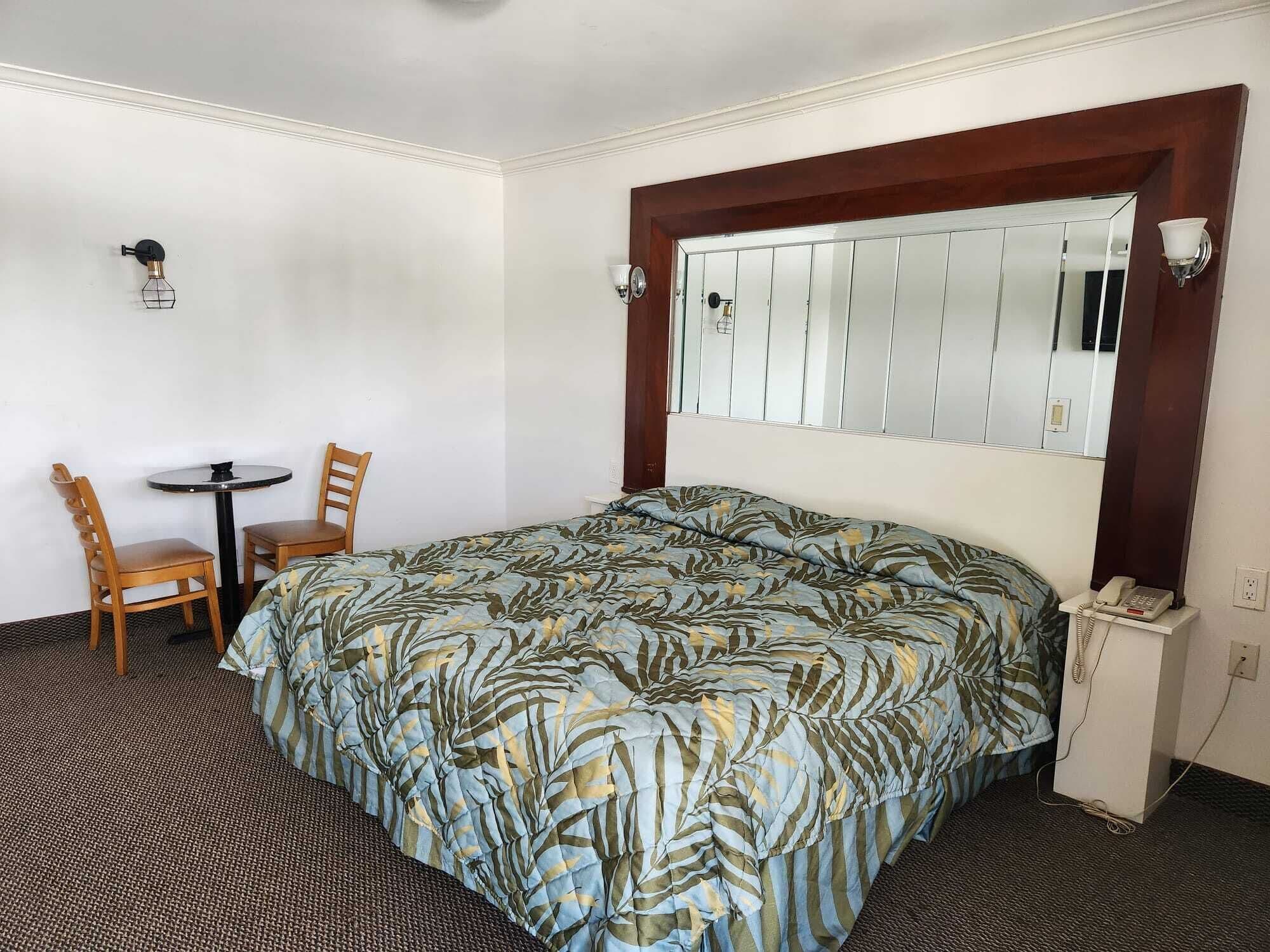 A hotel room with a bed, a small table with two chairs, a mirror, and a telephone.