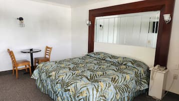 A hotel room with a bed, a small table with two chairs, a mirror, and a telephone.