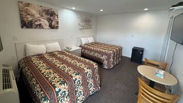 A hotel room with two beds, a small table, a chair, a heater, and a TV.