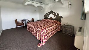 Habitación de hotel con cama, escritorio, silla, pequeña mesa, calefactor y espejo.