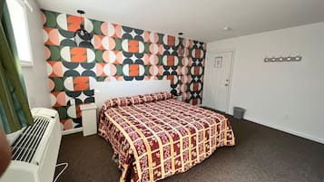 A hotel room with a patterned wall, a bed with a red and gold bedspread, a white radiator, and a door with a coat rack.
