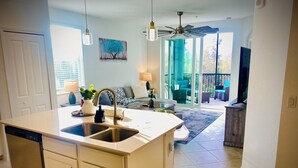 A modern kitchen with a central island, built-in dishwasher, and a large window providing natural light.