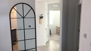 A hallway with a large arched mirror, a wooden cabinet with a plant, and a door leading to another room.