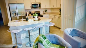 A modern kitchen with white cabinets, stainless steel appliances, and a bar area with stools.