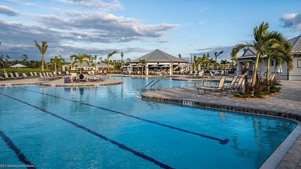 A swimming pool with lounge chairs and umbrellas, surrounded by palm trees and a pavilion.