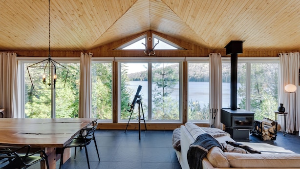 A cozy cabin interior with a dining area, a sofa, a telescope, and a wood-burning stove. - Repère tranquille au bord du lac (Saint-Alexis-des-Monts)