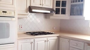 Cozinha com armários brancos, fogão a gás, micro-ondas e painel de azulejos.