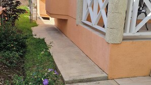 Uma casa com varanda, um jardim com flores roxas e um corrimão branco.