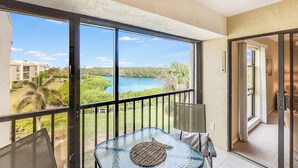 A balcony with a glass table, chairs, and a view of a lake and buildings.