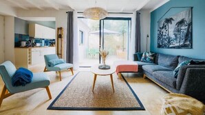 Una sala de estar moderna con un sofá, dos sillones, una mesa de centro y vistas de la cocina y un espacio exterior a través de amplios ventanales.