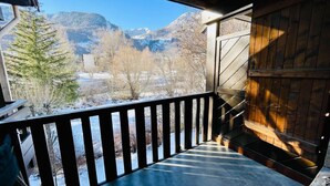 A wooden balcony with a view of snow-covered mountains and trees.