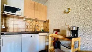 A compact kitchen with a microwave, two dishwashers, a coffee maker, and a wooden shelf.