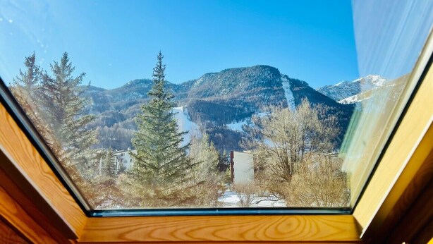 A view through a skylight of a mountainous landscape with trees and a building.