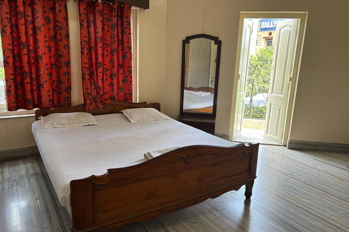 Ein Doppelbett mit weißen Leinen, einem hölzernen Kopfteil und roten floralen Vorhängen.
