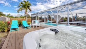 A hot tub with a wooden deck, surrounded by lounge chairs and a covered area.