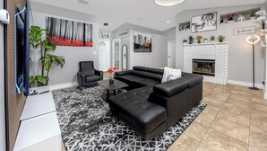 A modern living room with a sectional sofa, a flat-screen TV, a fireplace, and decorative plants.