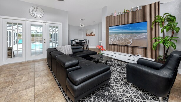 A modern living room with a sectional sofa, a black armchair, a coffee table, and a large flat-screen TV mounted on a wooden panel wall.
