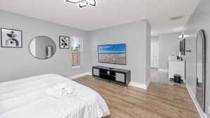 A modern bedroom with a large bed, a TV, a mirror, and a ceiling fan.