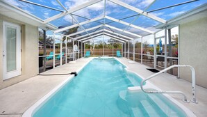 A covered swimming pool with a glass roof, surrounded by lounge chairs and a wooden fence.