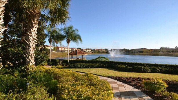 A landscaped area with a pathway, palm trees, and a body of water with a fountain. - Lovely 3 Bed Townhome in Encantada Resort-3036SLD (Kissimmee)