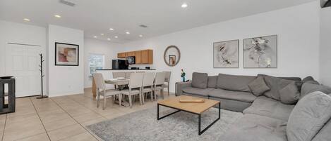 Una sala moderna con un sofá gris, una mesa de centro y una zona de comedor con una mesa y sillas.