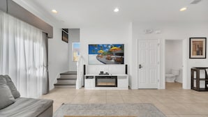 A modern living room with a grey sofa, a wooden coffee table, a flat-screen TV mounted on the wall, and a staircase leading to another room. - Lovely 3 Bed Townhome in Encantada Resort-3036SLD (Kissimmee)