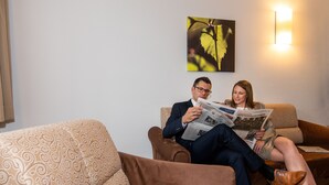 A man and a woman sitting on a brown sofa reading a newspaper. - Stadthotel Waidhofen an der Thaya (Waidhofen an der Thaya)