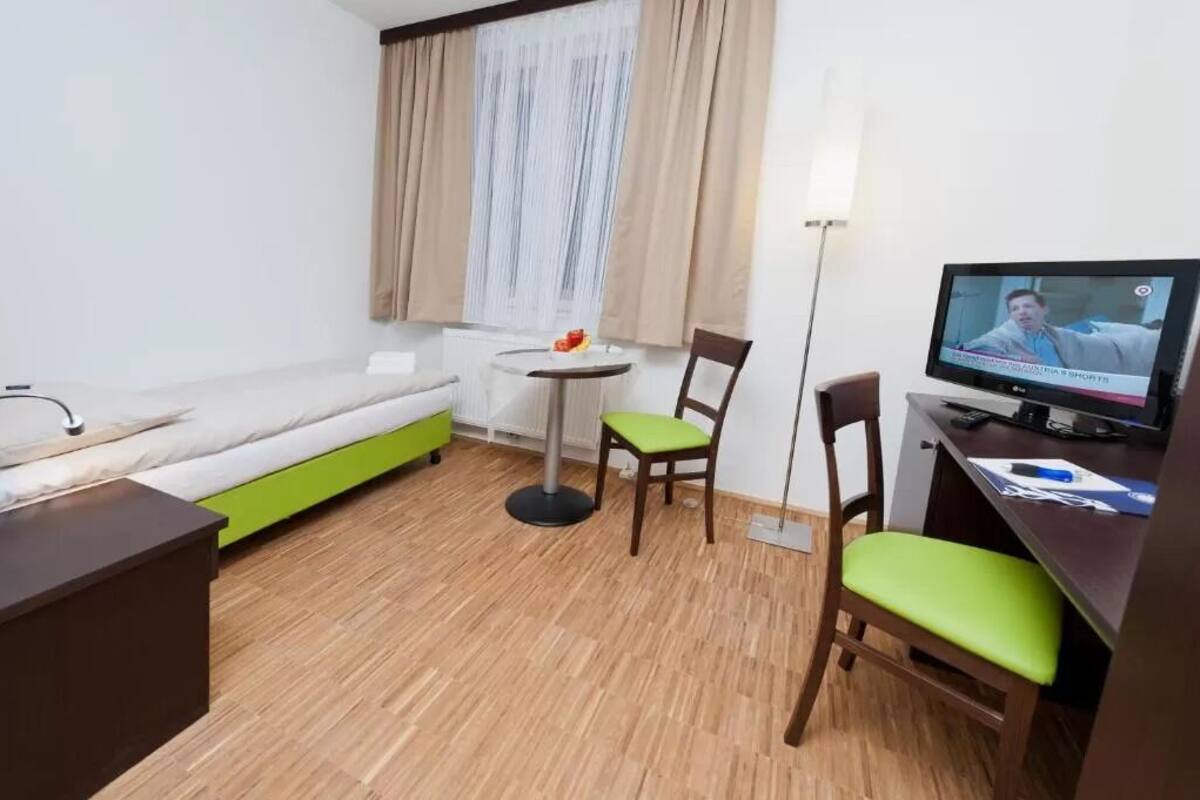 Une chambre d’hôtel de taille réduite, comprenant un lit, un petit bureau avec un ordinateur, une chaise, une table ronde et un téléviseur.