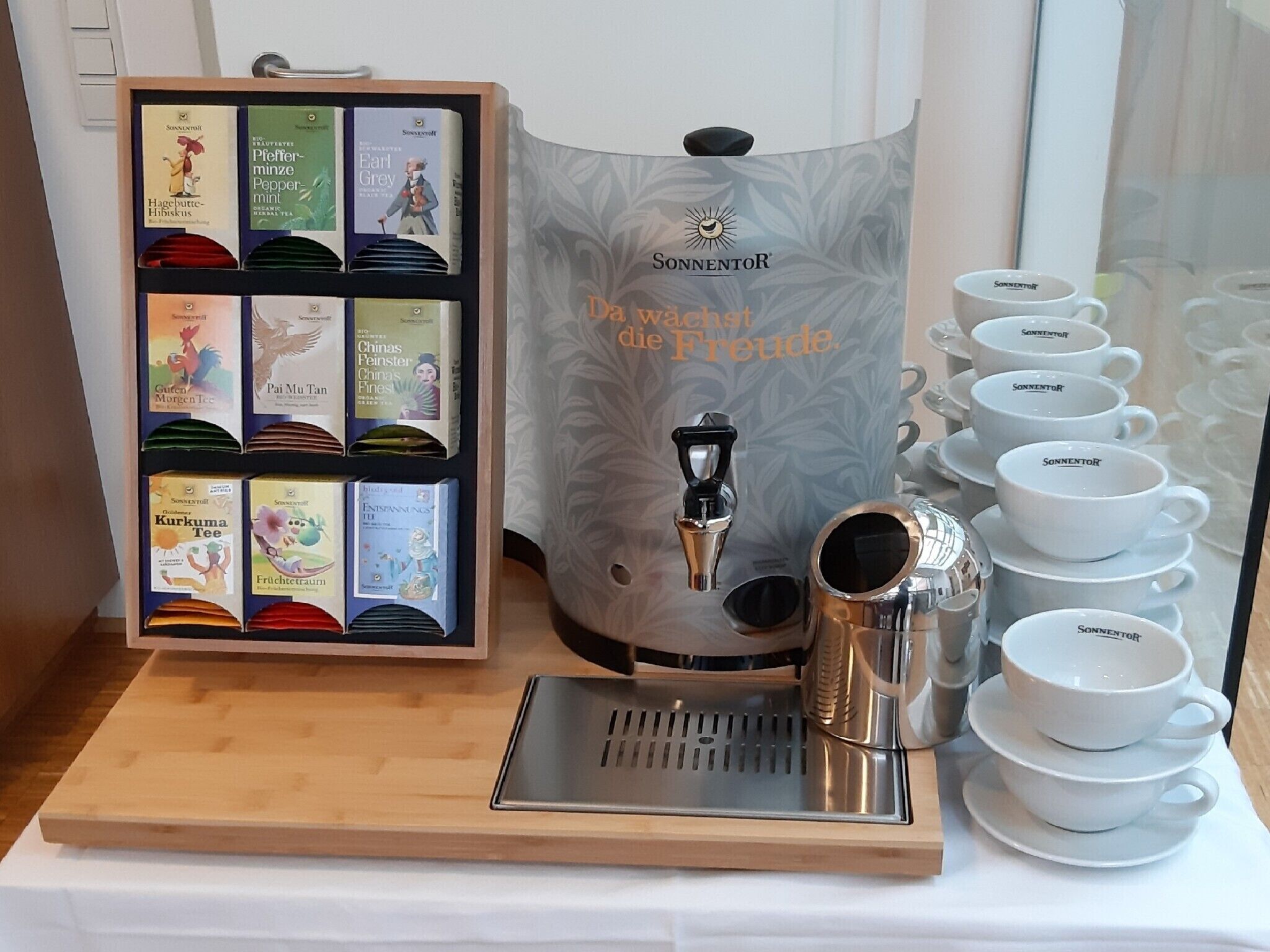 A coffee station with a coffee machine, a display of tea boxes, and a set of white cups.