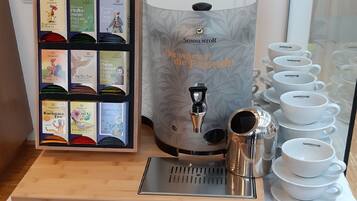 A coffee station with a coffee machine, a display of tea boxes, and a set of white cups.