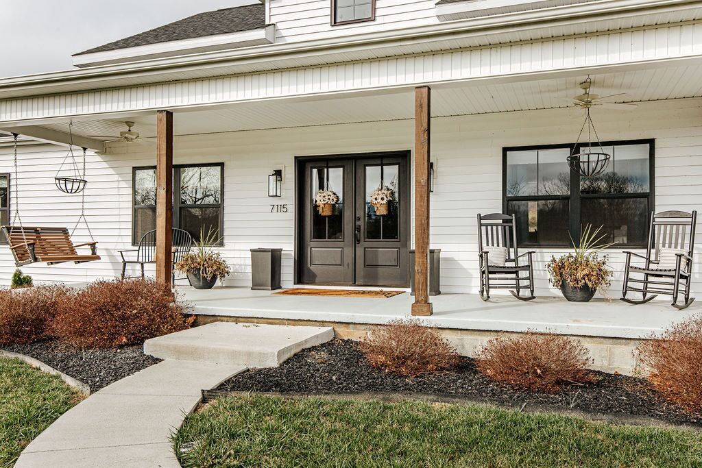 A white house with a porch, two doors, and a number '7115' on the wall.