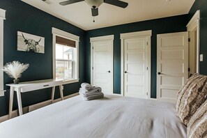 A bedroom with a bed, a desk, a ceiling fan, and a window.