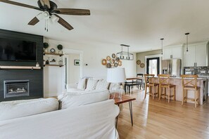 A spacious living room with a fireplace, a dining area, and a kitchen with wooden cabinets and a bar.