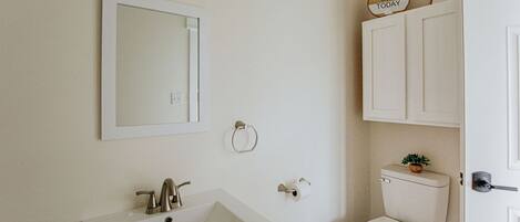 A bathroom with a white sink, mirror, toilet, and a cabinet with a small plant.