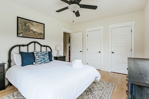 Un dormitorio con cama, ventilador de techo, un cuadro y puertas blancas.