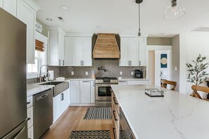 A modern kitchen with white cabinets, a central island, a stove, and a hanging light fixture.